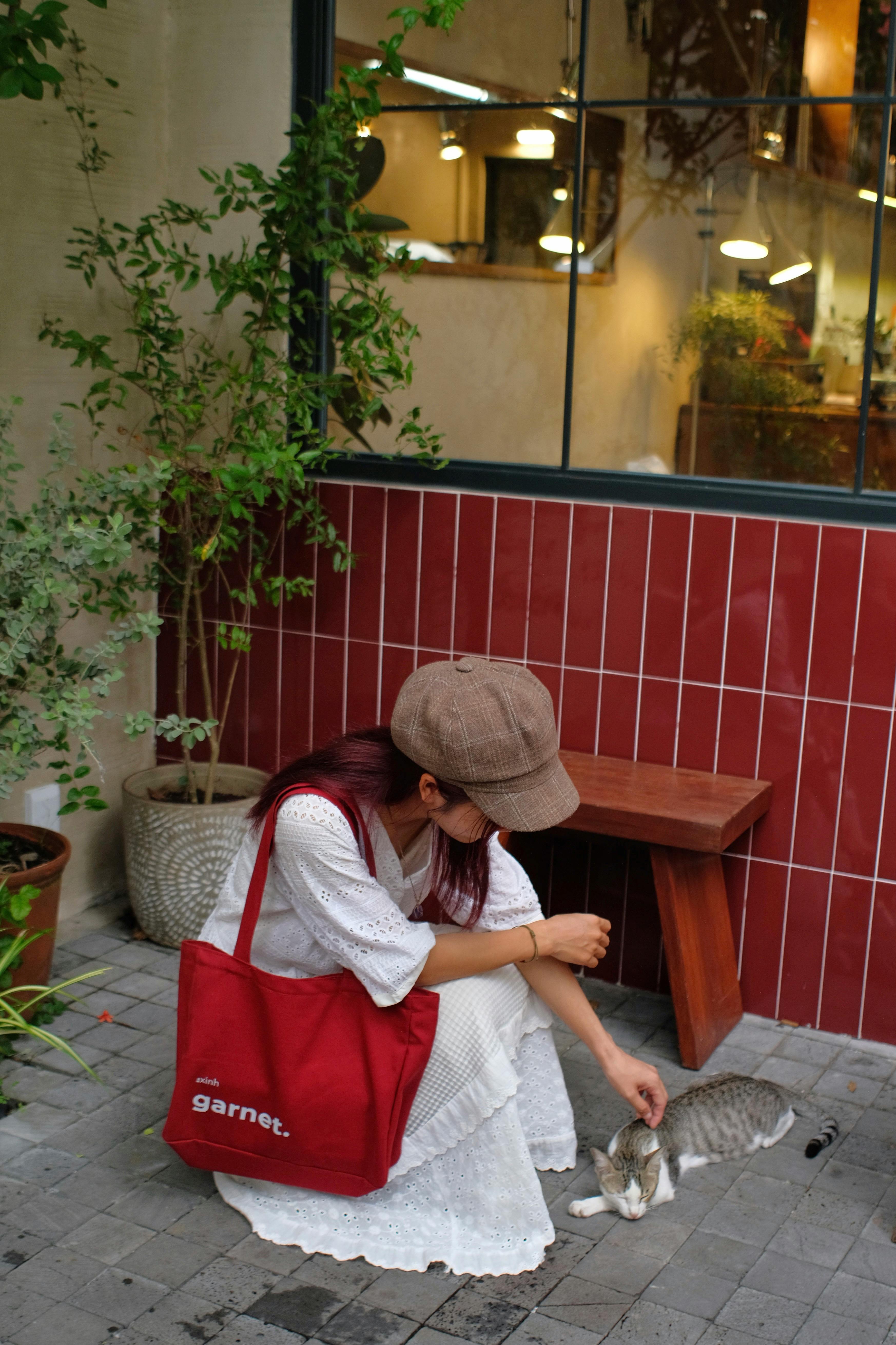 A woman in casual attire gently pets a cat outside a charming cafe, creating a serene and warm atmosphere.
