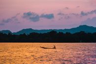 Peaceful sunset view with silhouette of a person canoeing on calm waters against a mountain backdrop.