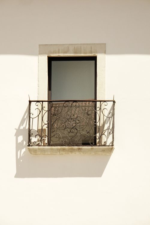 Free A minimalist photo of a decorative iron balcony casting a shadow on a plain wall in daylight. Stock Photo