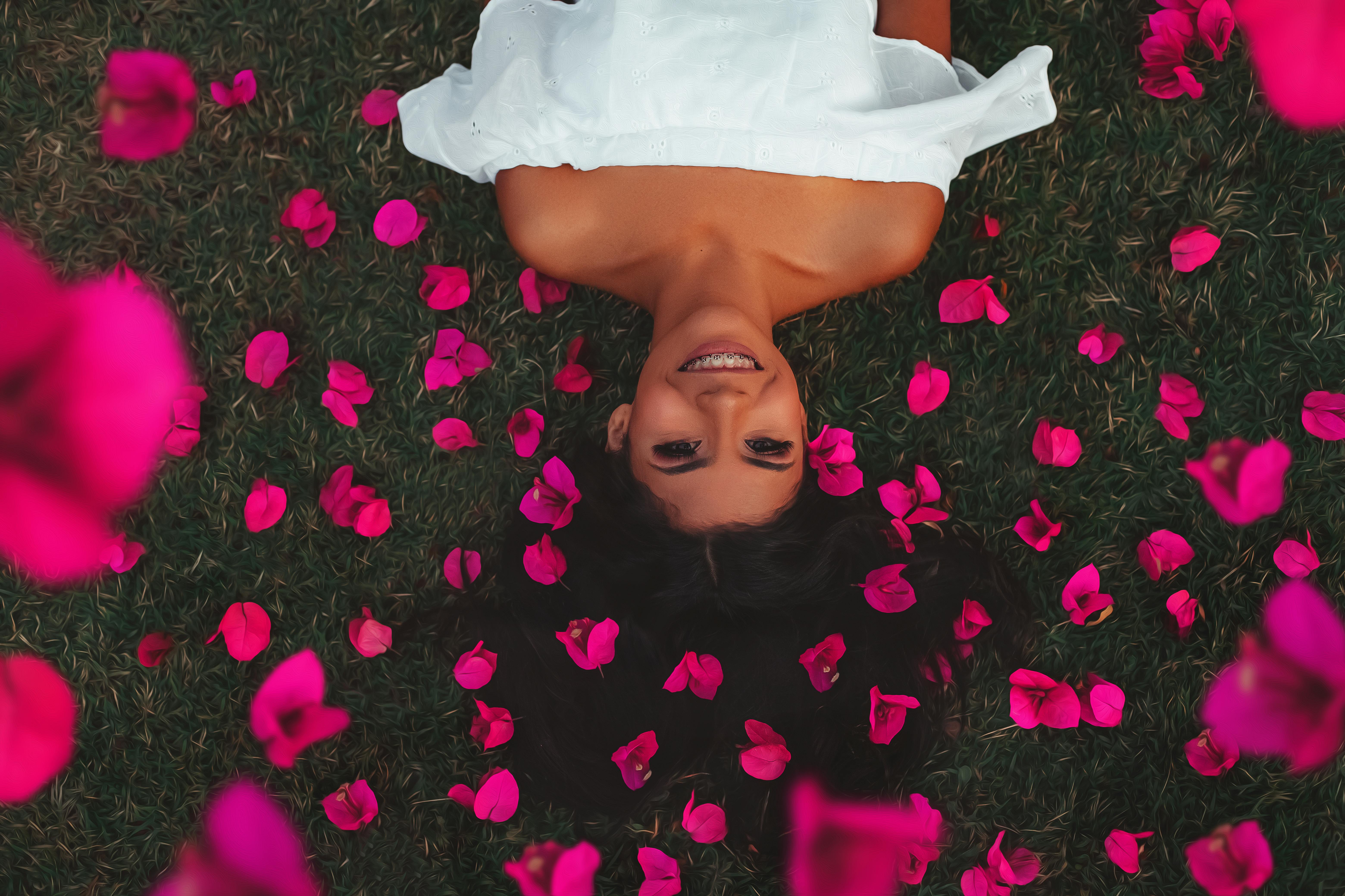 一位女子躺在落满粉色花瓣的草地上，微笑着