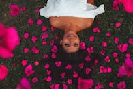 一位女子躺在落满粉色花瓣的草地上，微笑着