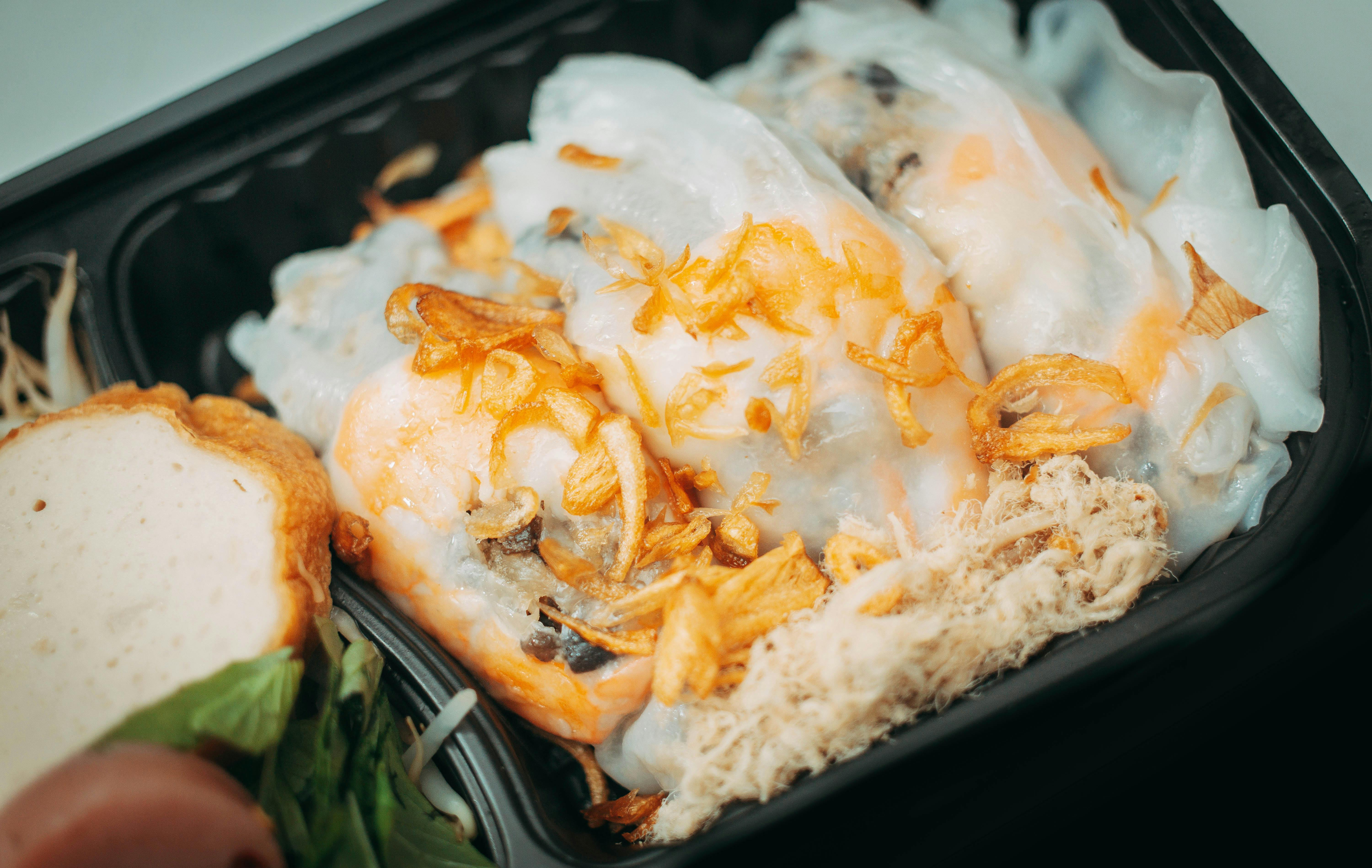 Close-up of Vietnamese Banh Cuon in a black tray with fried shallots and herbs.