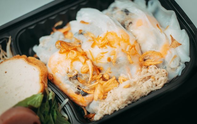 Close-up of Vietnamese Banh Cuon in a black tray with fried shallots and herbs.