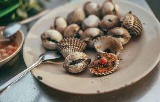 A delicious plate of cooked cockles served with sauce on the side, perfect for seafood lovers.