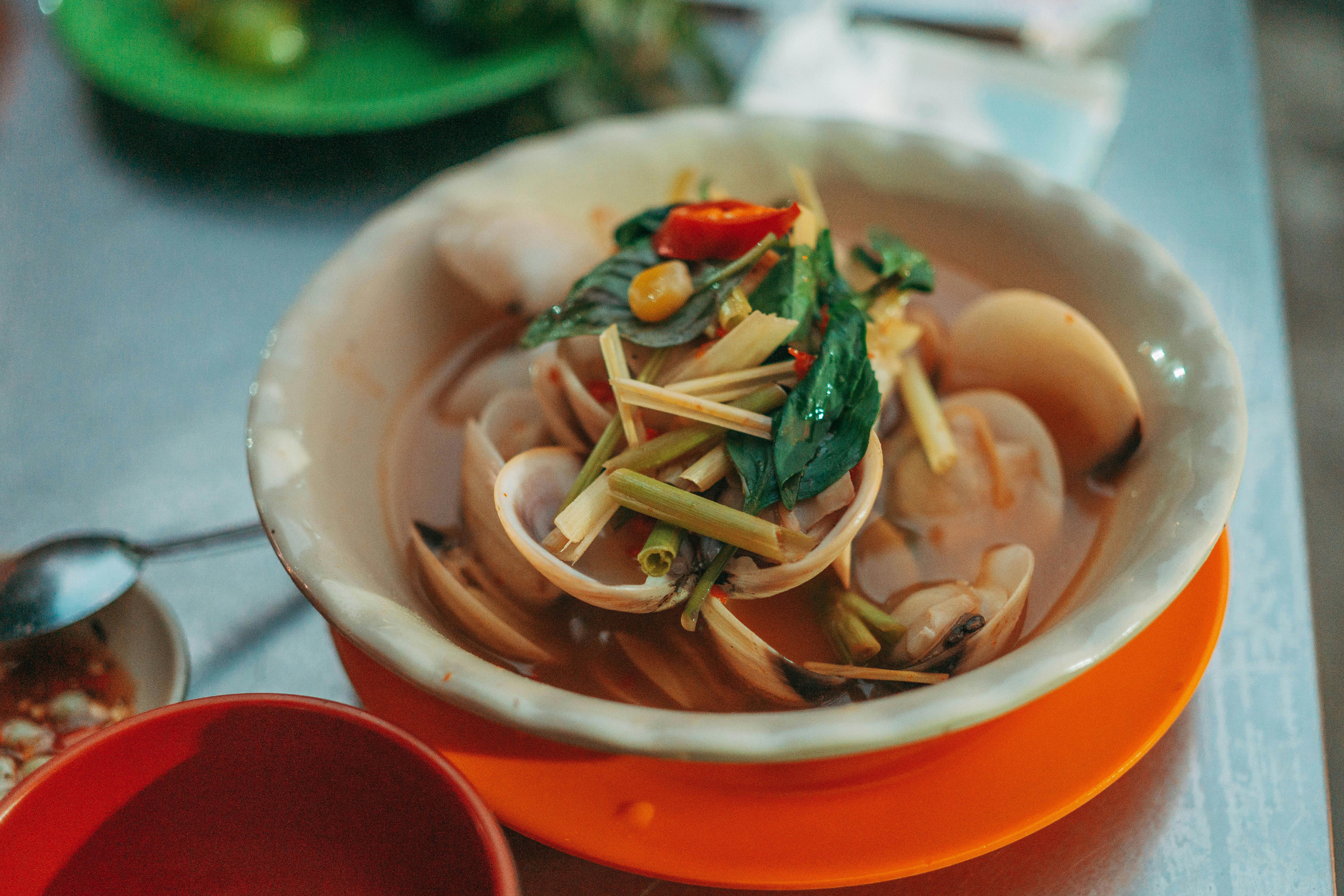 Delicious spicy clam soup garnished with lemongrass, chili, and herbs, served in a rustic bowl.
