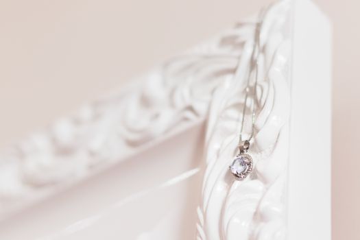 Close-up of a silver pendant necklace hanging on an ornate white frame. Perfect for jewelry and fashion themes.