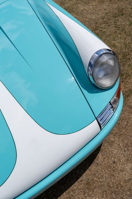 Close-up of a vintage turquoise car hood with classic headlights and a sleek design.