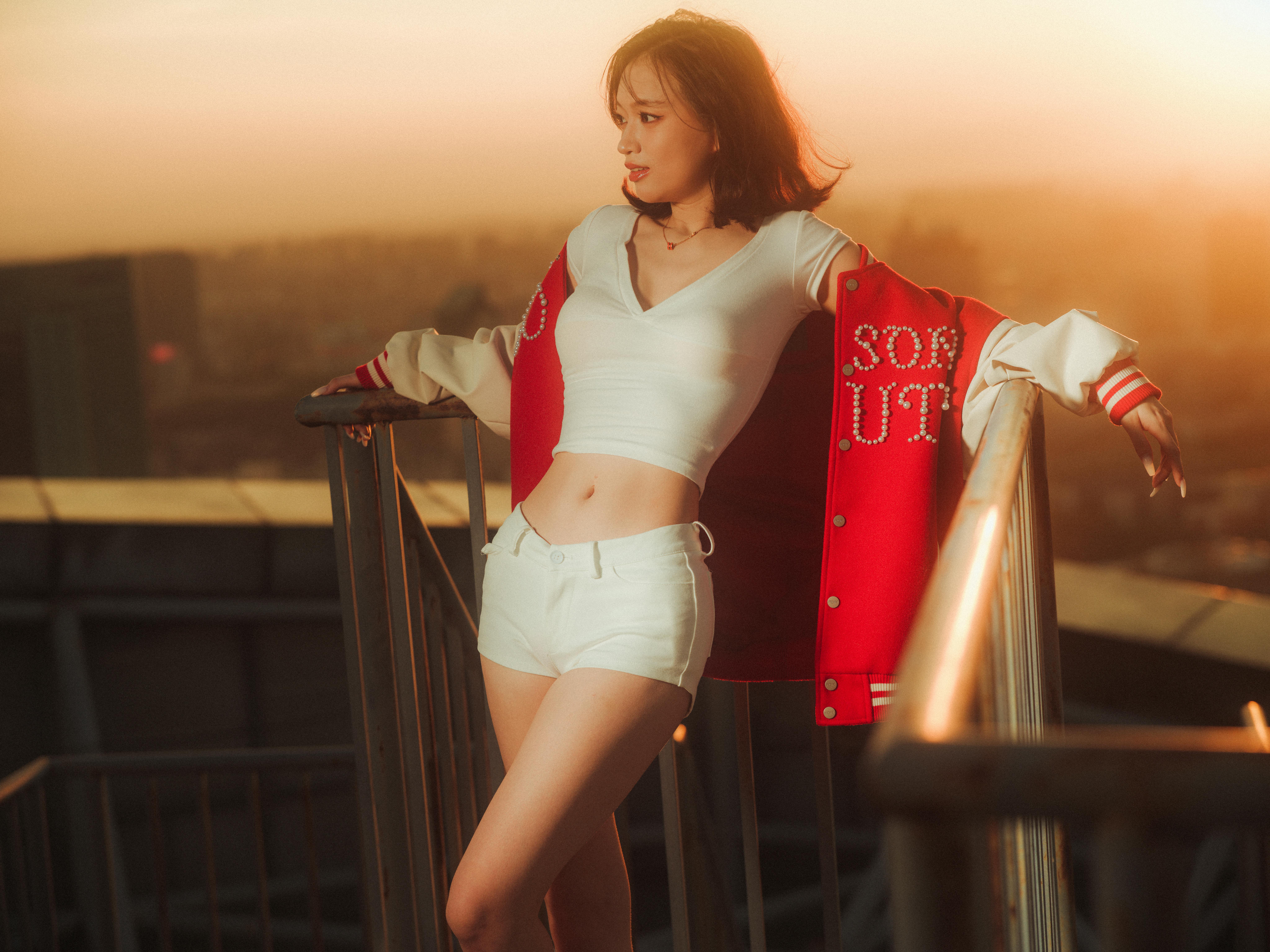Free Framed by golden sunset hues, a stylish woman in a red jacket poses confidently on a rooftop. Stock Photo