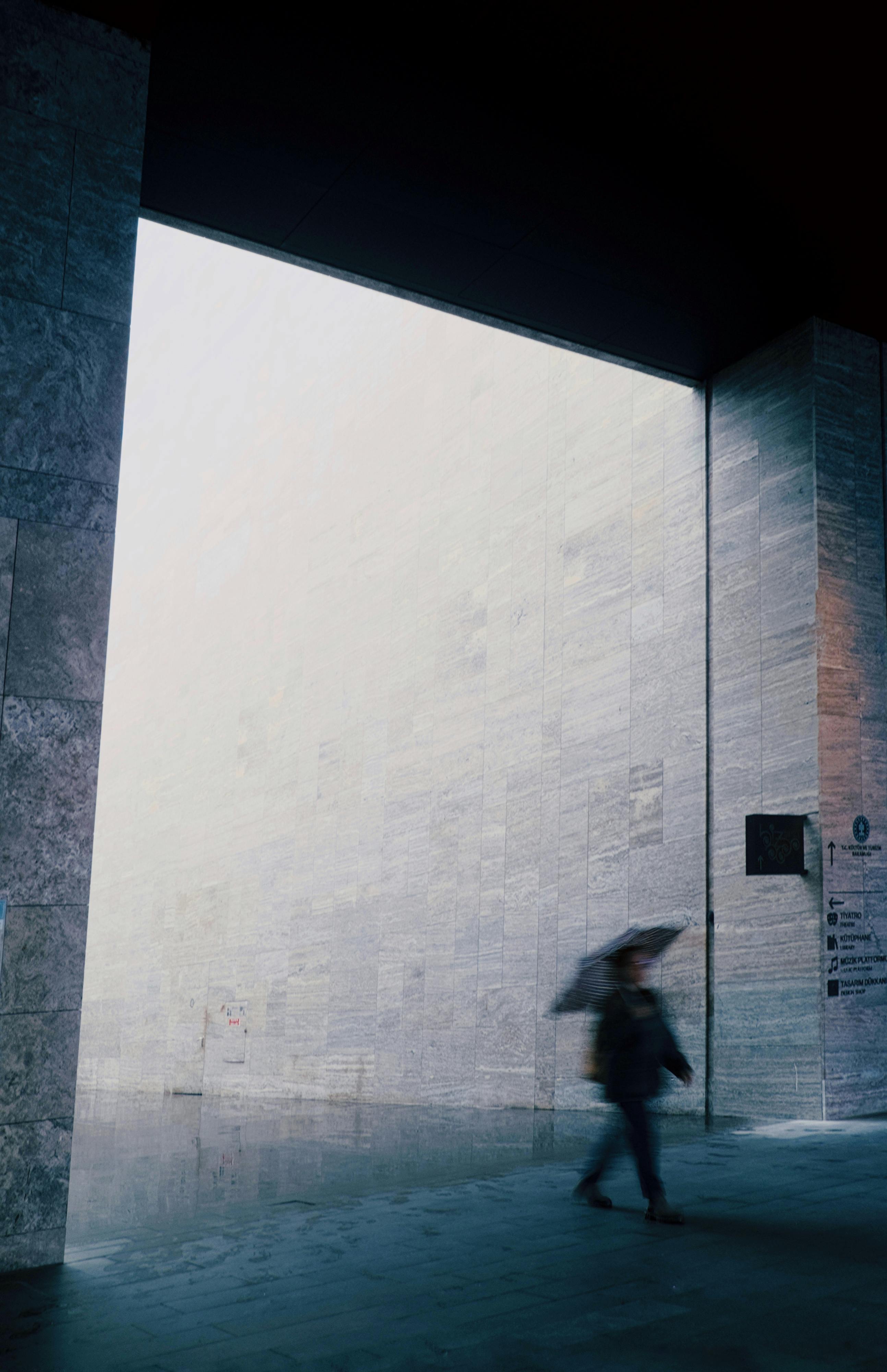 Blurred person with umbrella in minimalist urban setting, capturing rainy day mood.