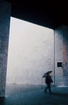 Blurred person with umbrella in minimalist urban setting, capturing rainy day mood.