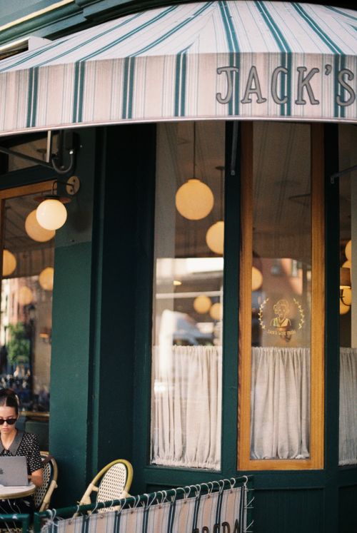 Free Outdoor cafe with striped awning, round lights, and a person working on a laptop. Stock Photo