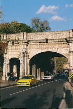 Yellow taxi driving under a historic bridge in Istanbul, Turkey.