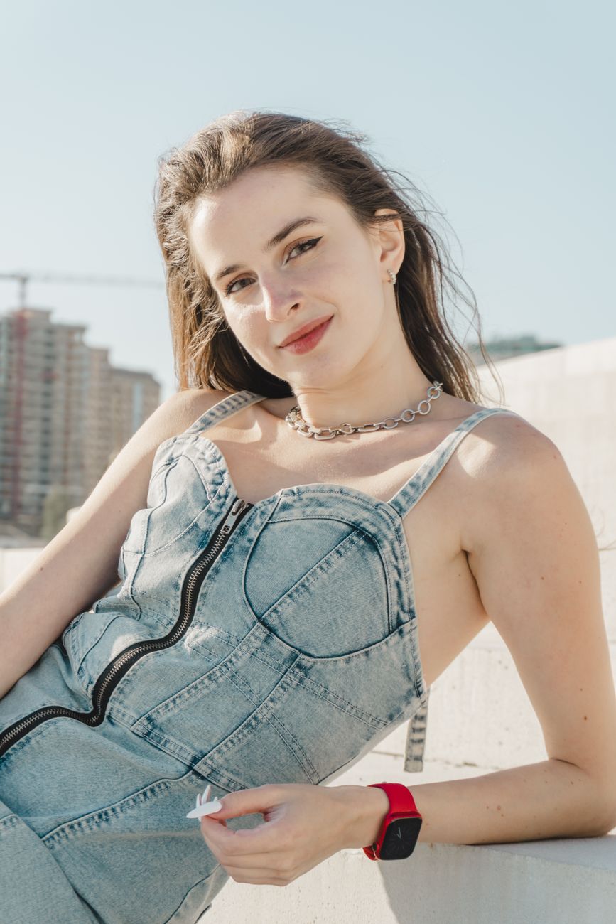 Young woman in denim outfit smiles confidently outdoors on a sunny day, showcasing modern fashion.