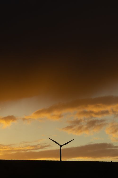Free Silhouette of a wind turbine against a vibrant sunset sky, creating a dramatic scene. Stock Photo