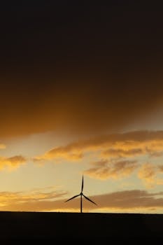 Silhouette of a wind turbine set against a vibrant sunset sky with dramatic clouds.