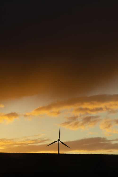 Free Silhouette of a wind turbine set against a vibrant sunset sky with dramatic clouds. Stock Photo
