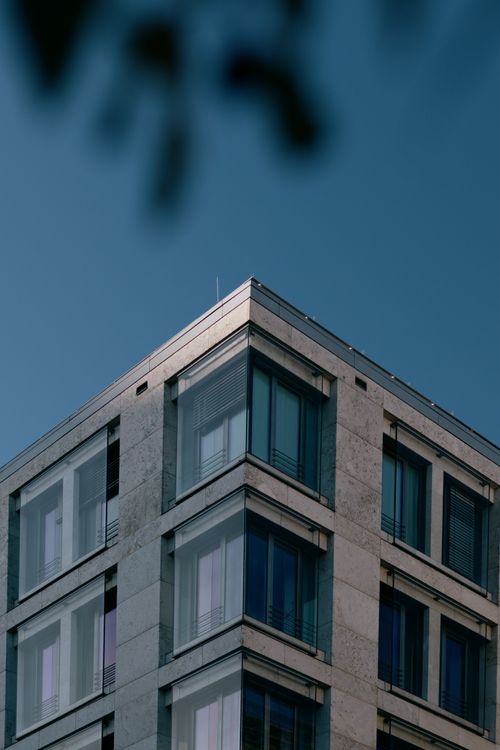 Free A modern angular building with glass windows in urban setting against a blue sky. Stock Photo