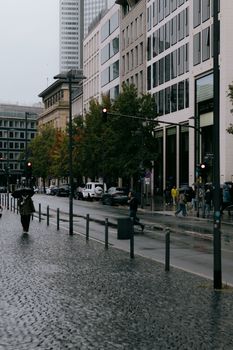 Urban cityscape in Frankfurt featuring modern architecture and pedestrians in the rain.