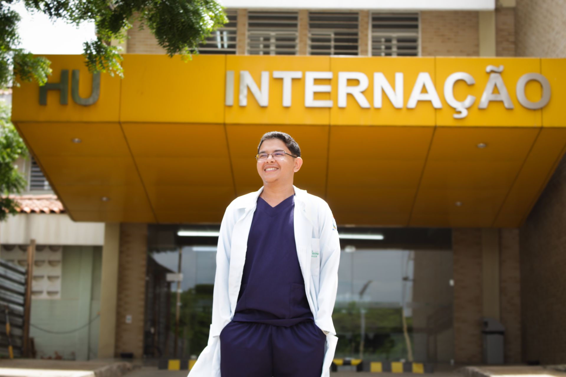Smiling medical professional stands at the entrance of a hospital with Internação sign.