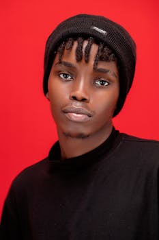 Modern portrait of a young man in a black beanie against a vibrant red background, expressing calm confidence.