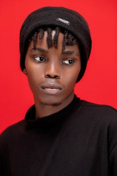 Portrait of a young man in black attire and beanie against a vivid red background.