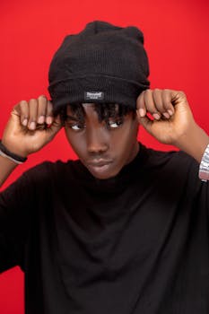 Portrait of a fashionable young man wearing a black beanie, posing against a red backdrop.