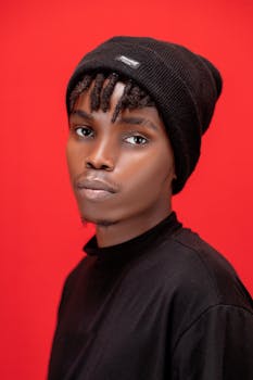 Striking portrait of a young man wearing a black beanie and shirt against a red backdrop.