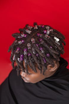 Close-up of a fashionable beaded hairstyle against a bold red backdrop, showcasing artistic flair.