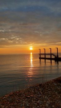 Beautiful sunset over a calm ocean with a pier and golden reflections, creating a peaceful and tranquil scene.