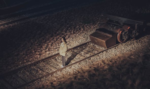 夜晚，一个女人孤独地站在灯火通明的铁轨旁，显得格外孤寂