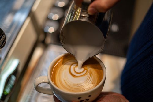 Free Hand pouring milk to create latte art in a coffee cup. Stock Photo
