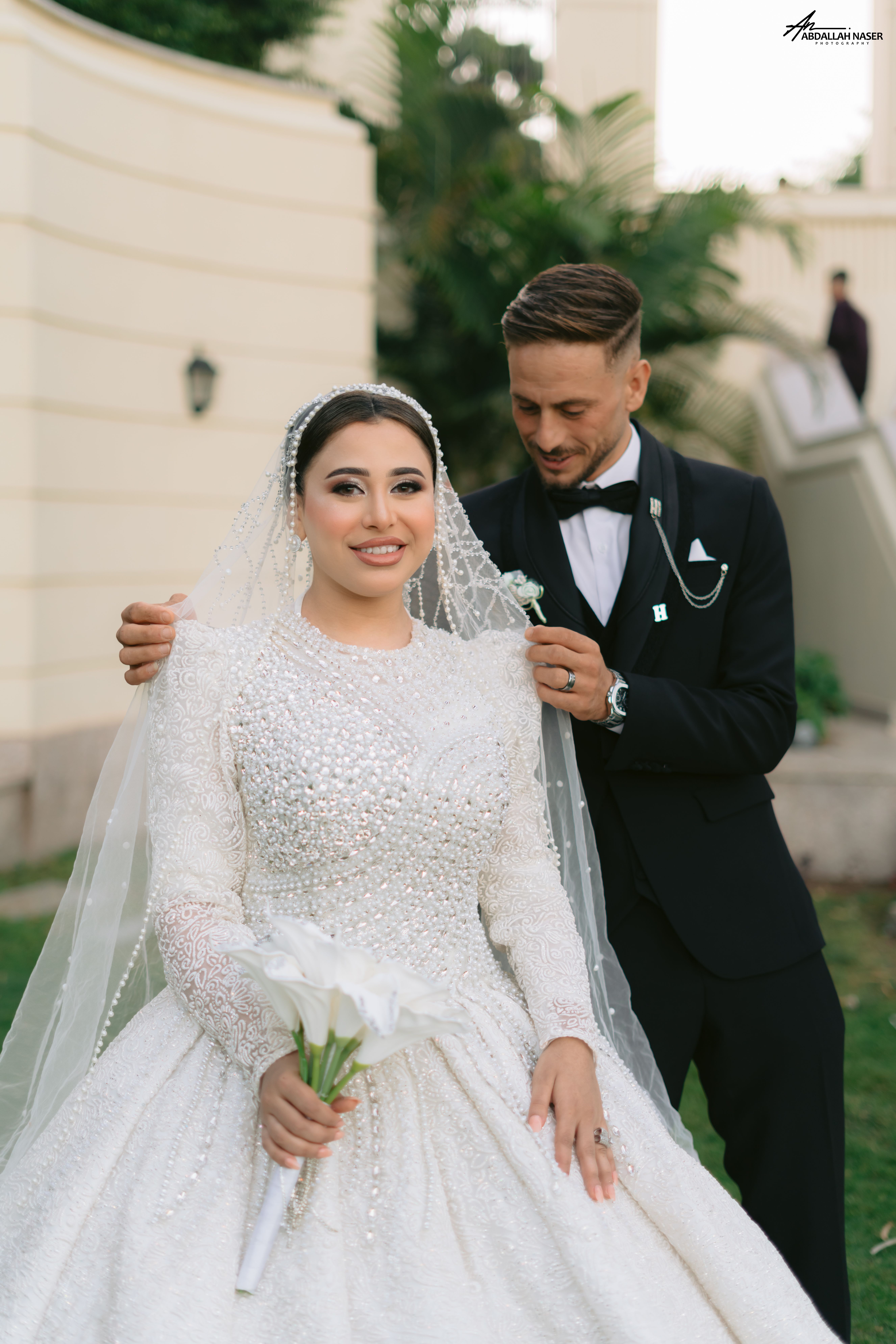 Charming wedding couple outdoors, bride in elegant gown, groom adjusting details.
