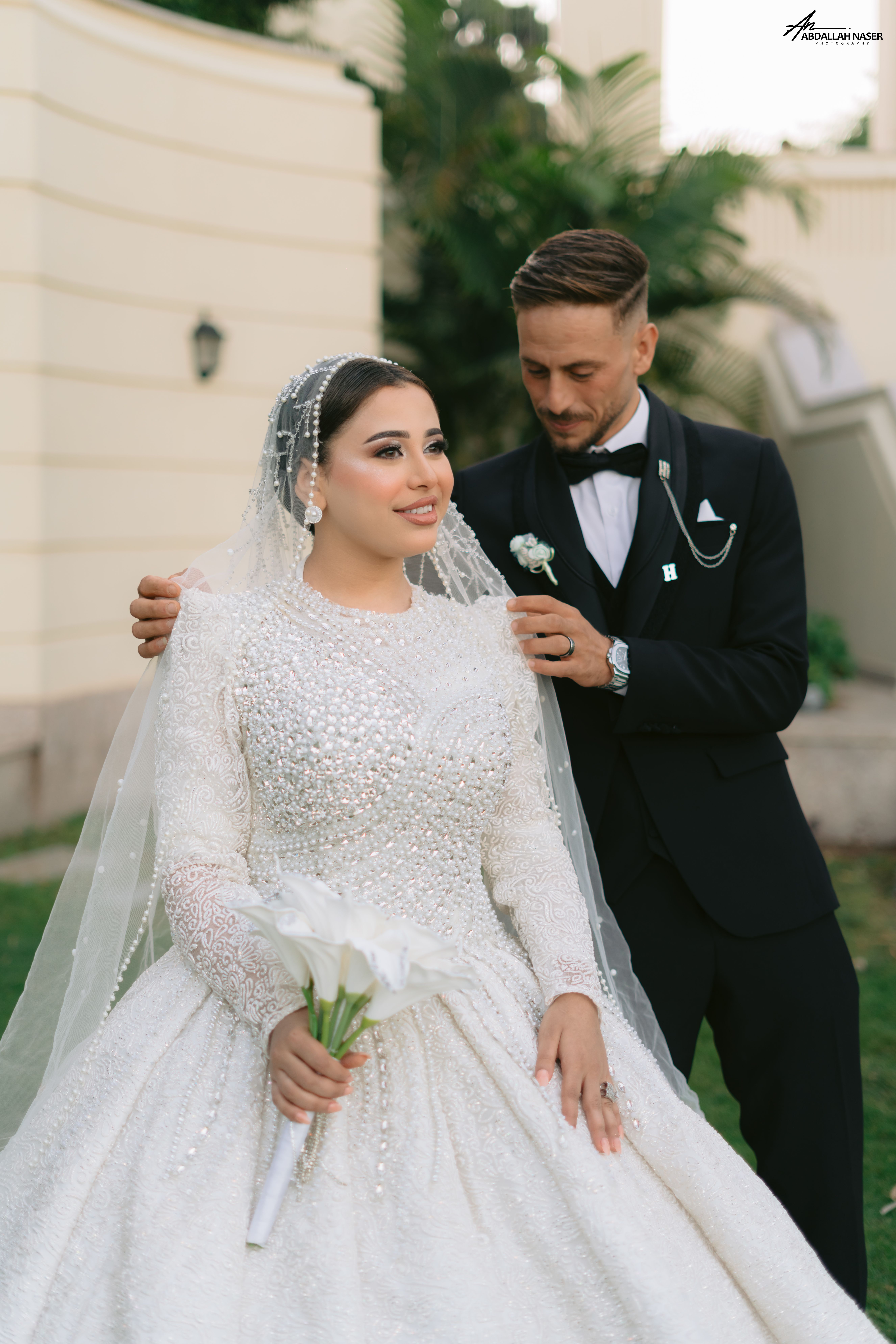 A joyful couple poses in wedding attire in an outdoor garden setting.