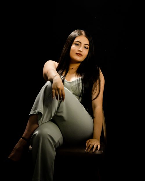 Free Portrait of an adult woman sitting confidently in elegant attire with a black backdrop. Stock Photo