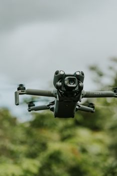 A detailed view of a drone hovering outdoors against a blurred natural background, showcasing modern technology.