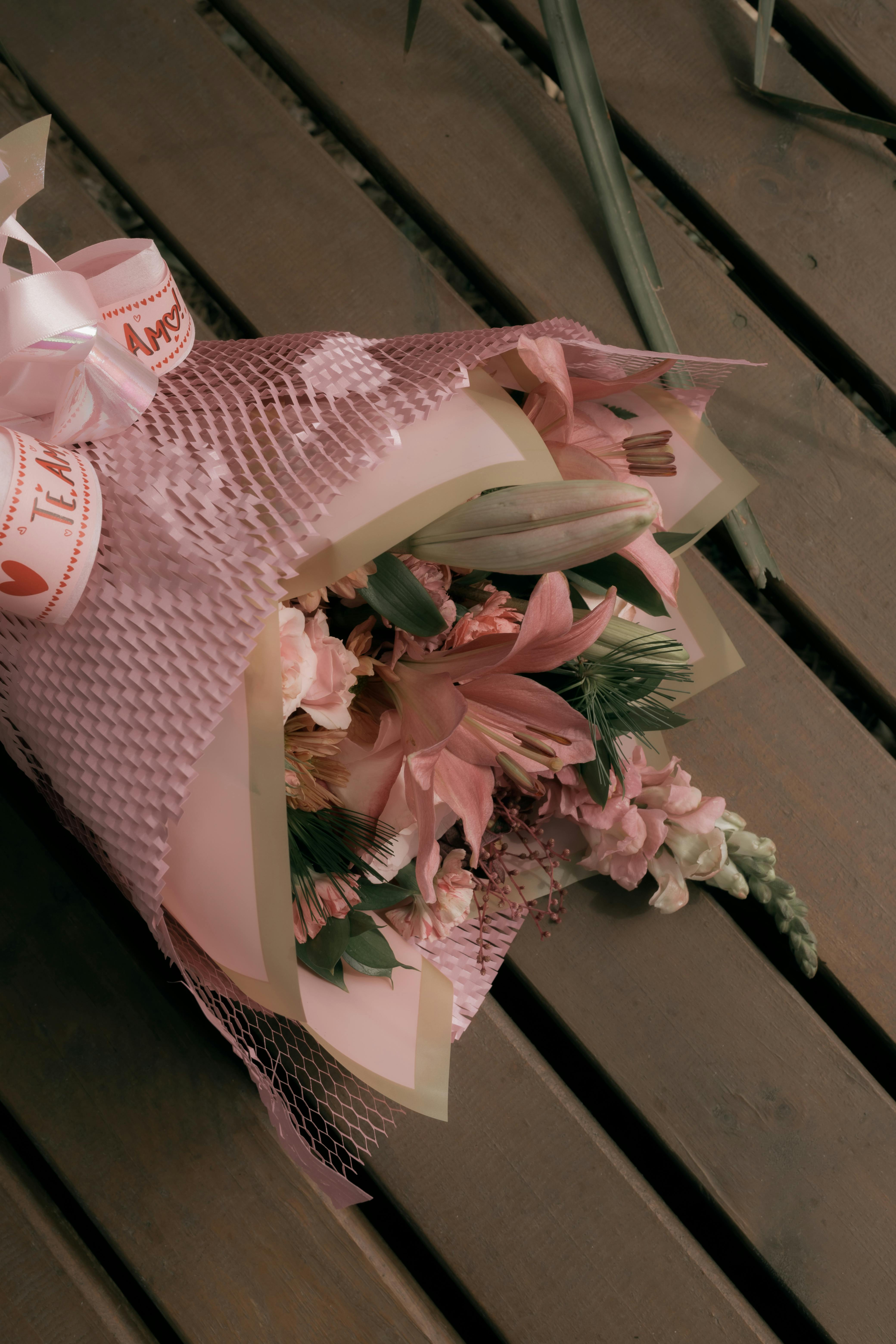 Charming pink flower bouquet artfully wrapped in mesh rests on a wooden table.