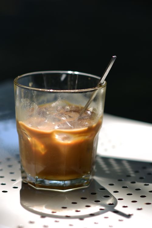 Free Glass of iced coffee on a sun-dappled table with a straw, exuding refreshing vibes. Stock Photo