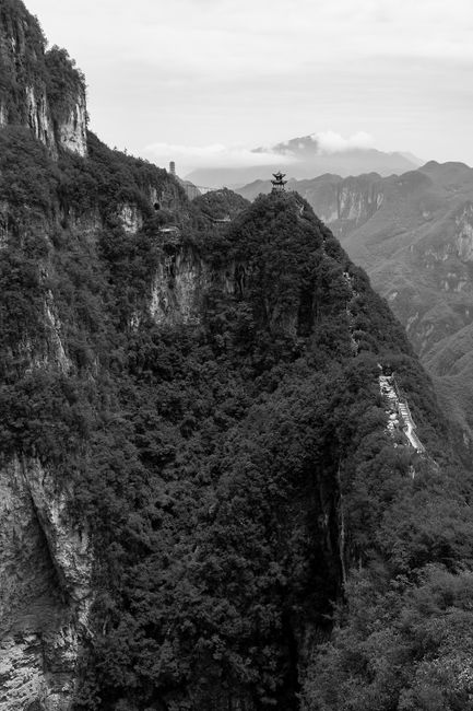 Black and white photo capturing a dramatic mountain landscape with dense forests and rugged cliffs.