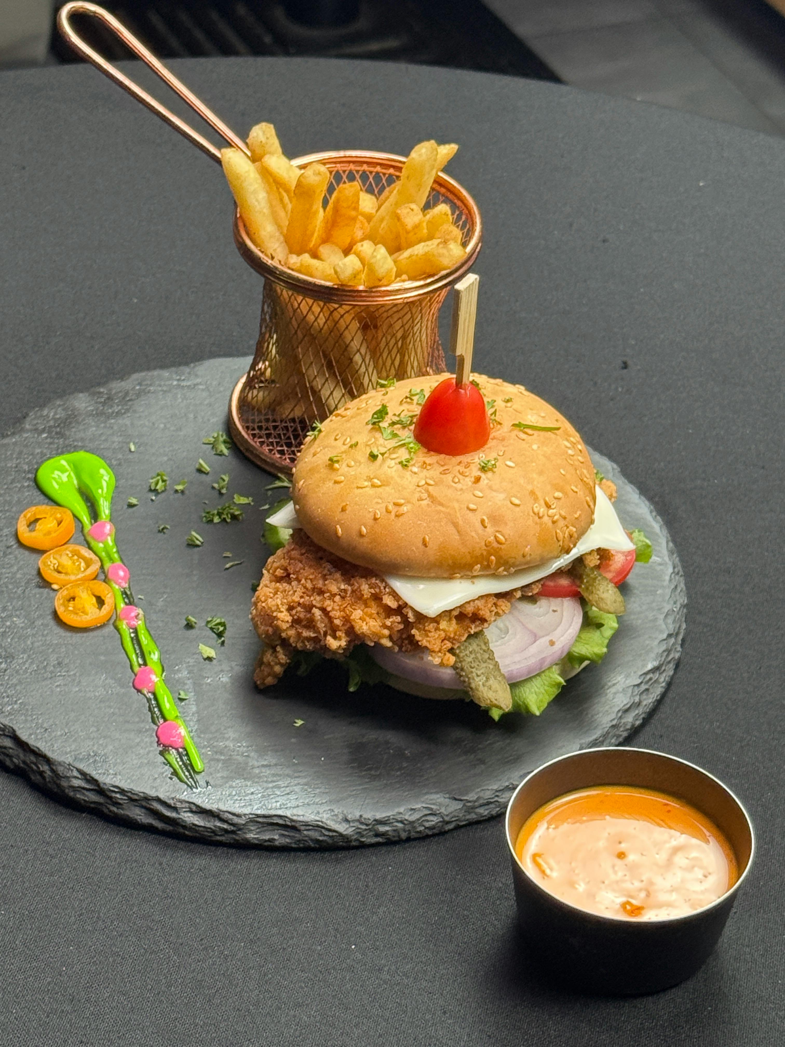 Sabrosa hamburguesa de pollo con papas fritas y una guarnición de salsa, elegantemente emplatada.