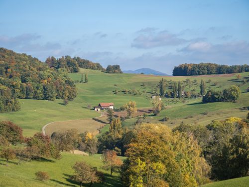 Free Beautiful countryside with rolling hills and a small farmhouse surrounded by lush greenery. Stock Photo