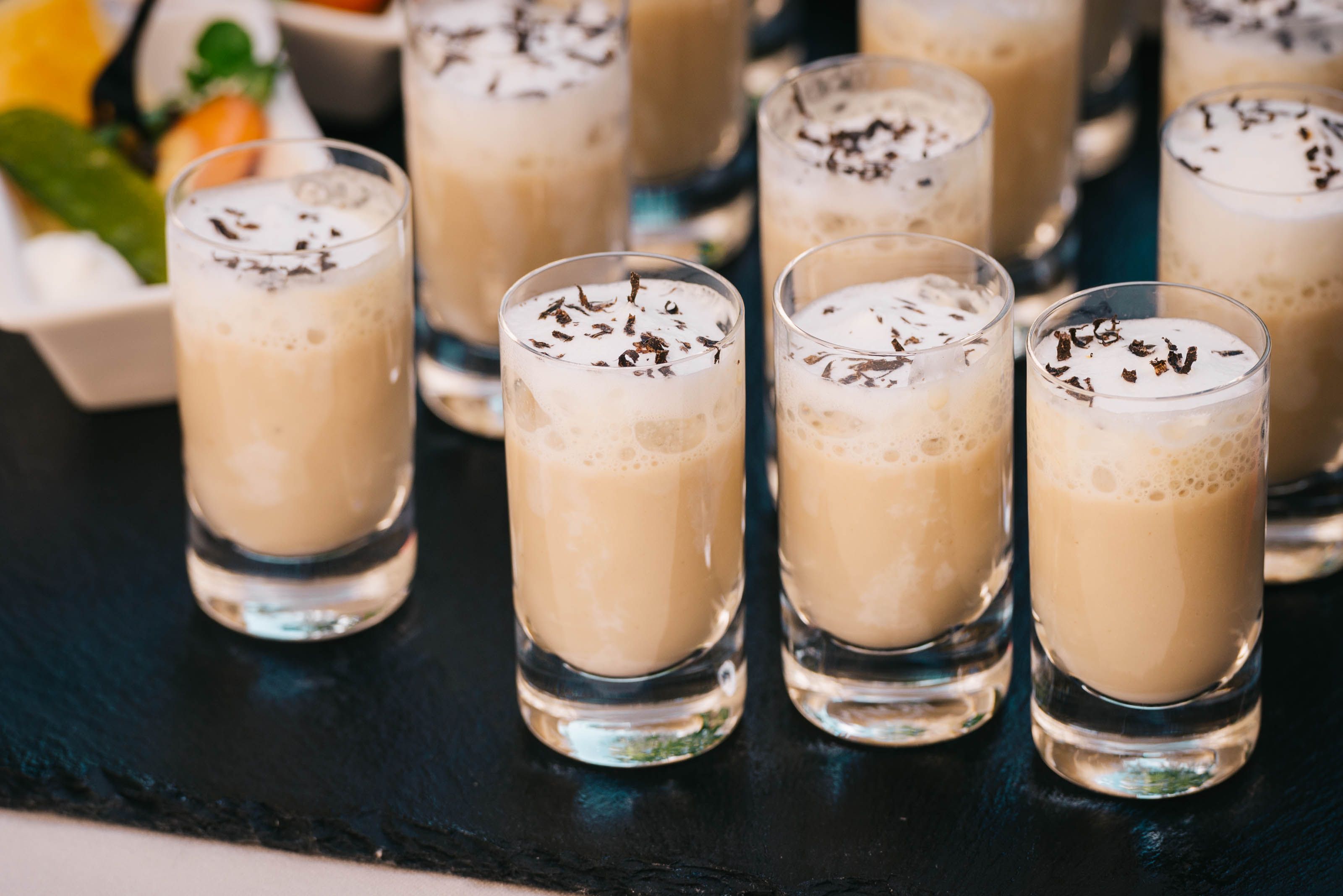 Close-up of creamy latte shots with a frothy top served in short glasses on a slate surface.
