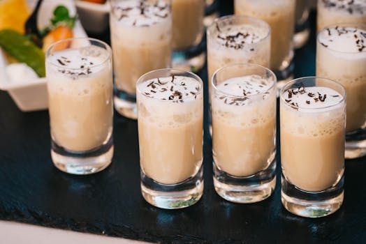 Close-up of creamy latte shots with a frothy top served in short glasses on a slate surface.