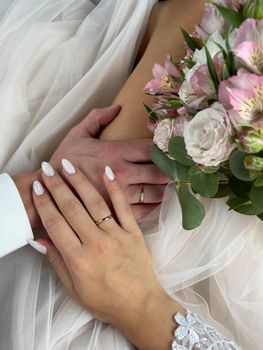Hands of a newlywed couple showing wedding rings alongside a delicate bouquet.