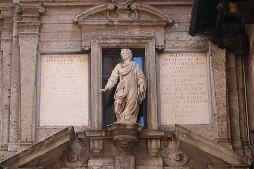 Close-up of ancient Roman statue with Latin inscriptions on historical building facade.