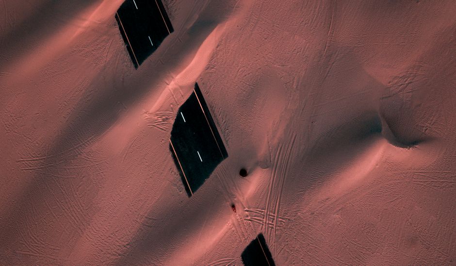 Drone capture of a road partially covered by sand dunes in a desert landscape.