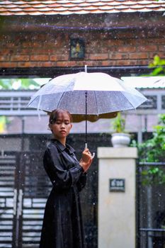 A serene portrait of a woman with an umbrella in rainy Hue, Vietnam.