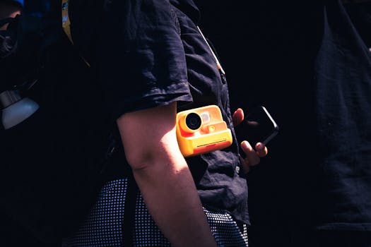 A stylish street scene in Dublin showing a person holding a yellow instant camera and a smartphone.