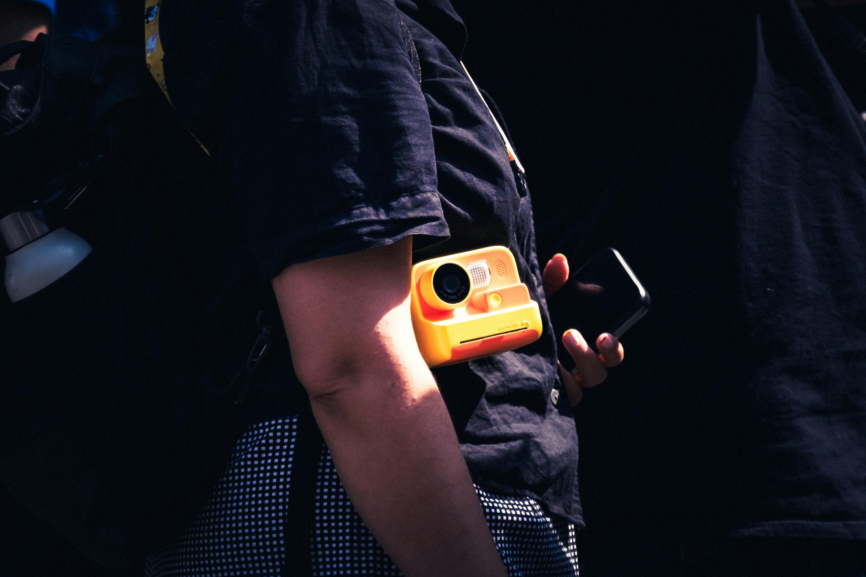 Gratis Una elegante escena callejera en Dublín que muestra a una persona sosteniendo una cámara instantánea amarilla y un teléfono inteligente. Foto de stock