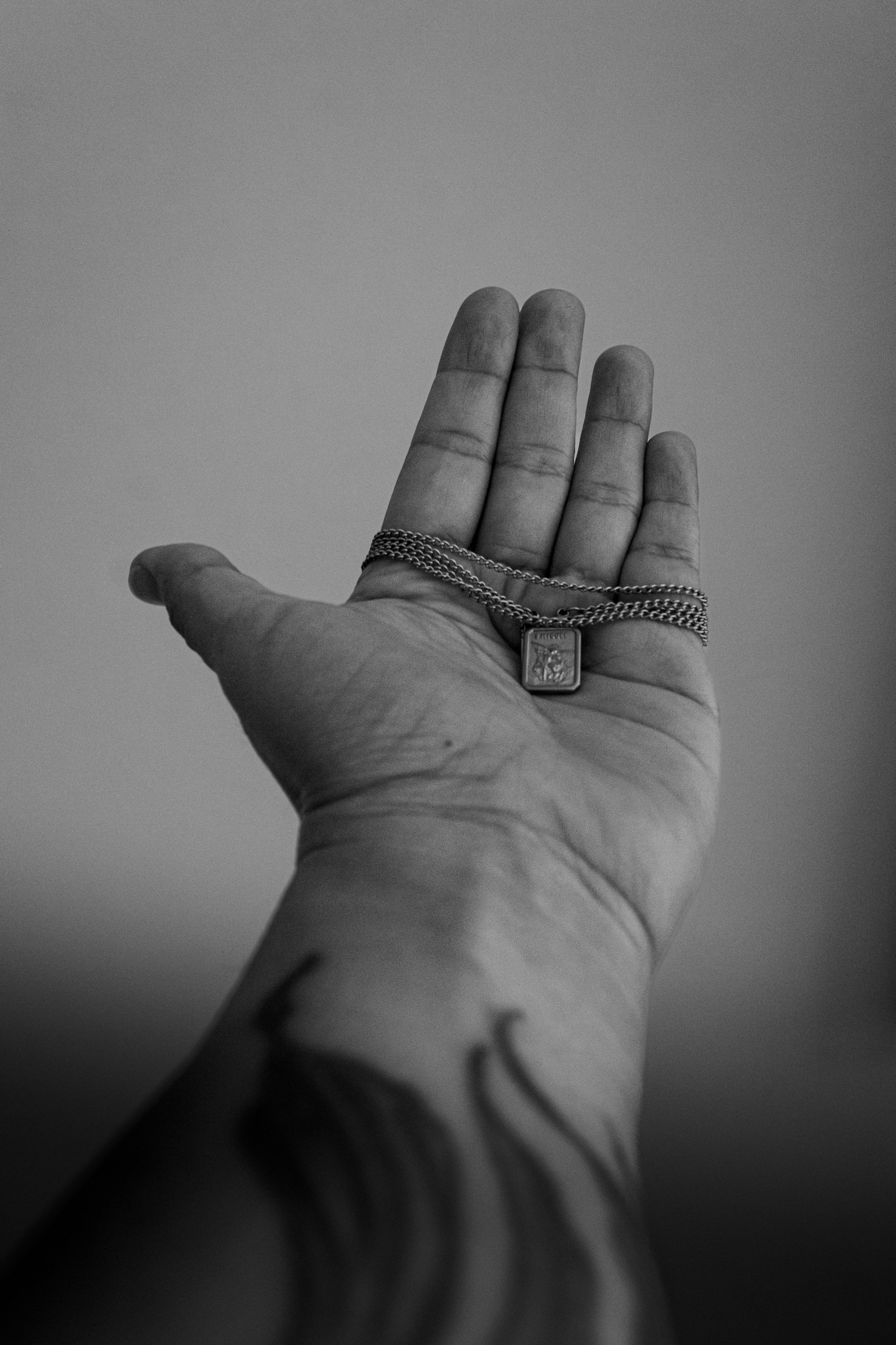 Ücretsiz Stil ve zarafeti simgeleyen kolyeli bir zincir tutan dövmeli elin tek renkli görüntüsü. Stok Fotoğraflar