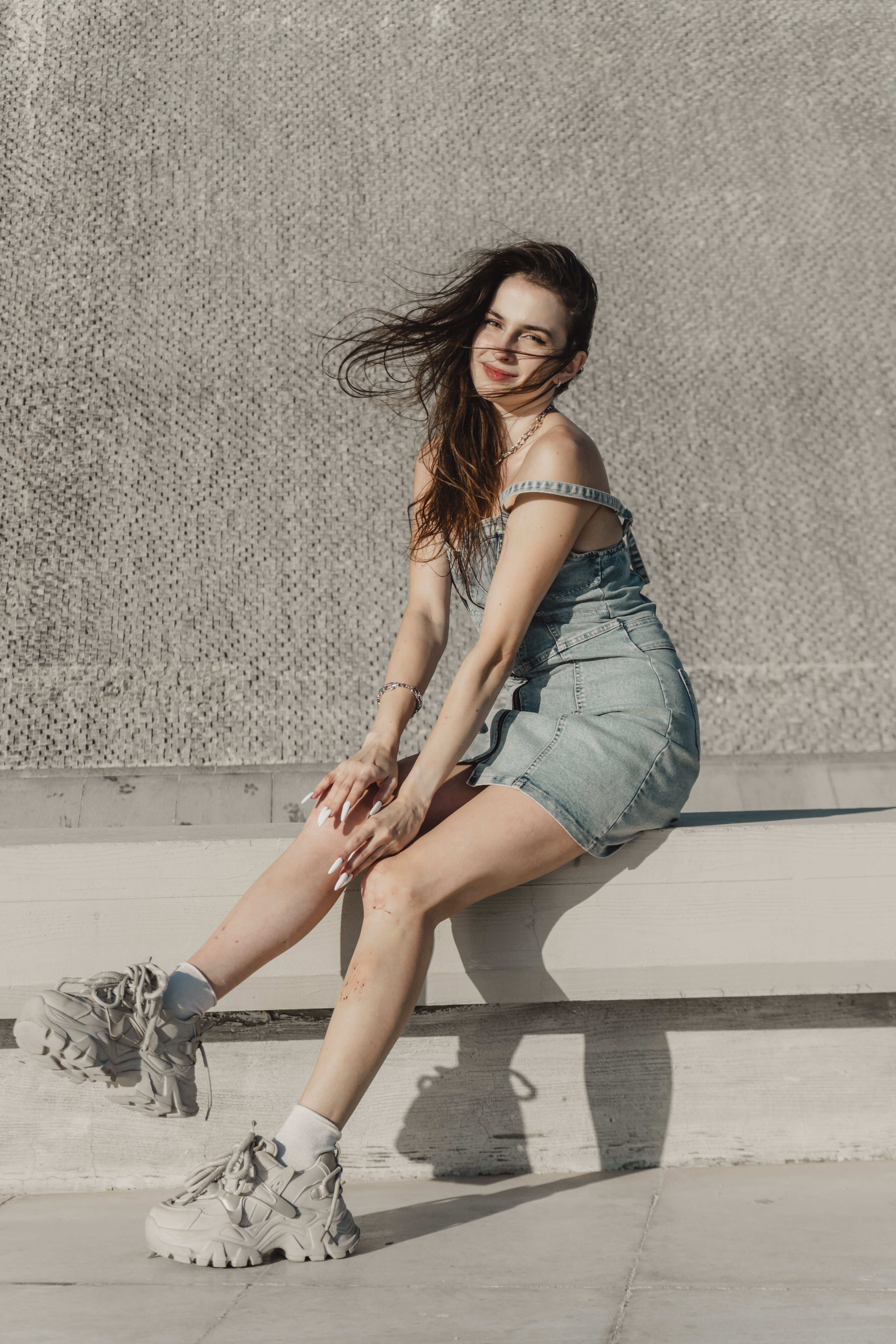 Young woman in casual outfit enjoying a sunny day outdoors, with a stylish denim dress and chunky sneakers.